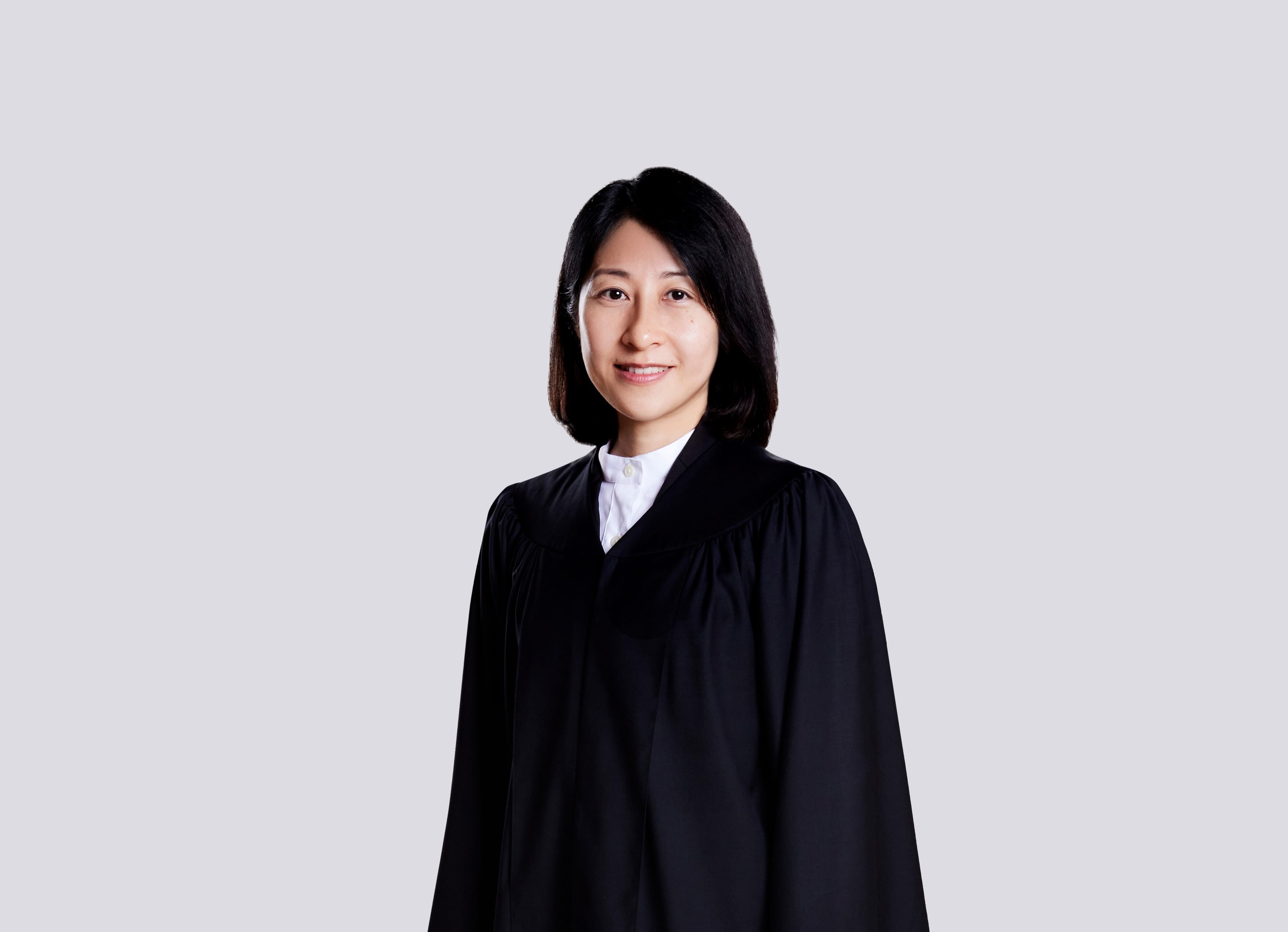 A person in a black graduation gown with a white shirt, against a light gray background.